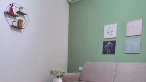 Moderni olohuone, jossa on vihreä seinä, beigenvärinen sohva, valkoinen sivupöytä, jossa on kasvi, sekä kuusikulmainen hylly, jossa on koriste-esineitä.