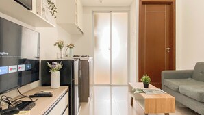 A modern living room with a flat-screen TV, a wooden coffee table, a grey sofa, and a sliding glass door leading to a balcony. - Trendy 1Br At Apartment Vittoria Residence (Jakarta)