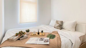A neatly made bed with white linens, a beige throw blanket, and a tray with small plants and a candle. - Trendy 1Br At Apartment Vittoria Residence (Jakarta)