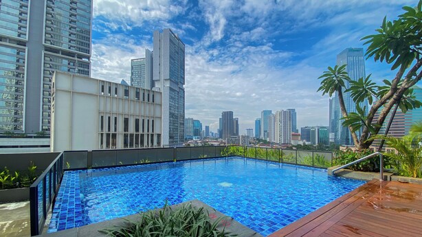 Une piscine sur le toit offrant une vue panoramique sur les gratte-ciel de la ville, entourée de bâtiments modernes et de palmiers.