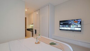 Una habitación de hotel moderna con una cama, un televisor de pantalla plana montado en la pared y vistas al área de la cocina contigua.