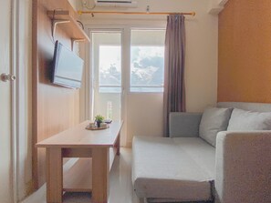 A small, compact room with a bed, a table with a plant, and a TV mounted on the wall. - Good And Homey 2Br Apartment At Green Pramuka City (Jakarta)