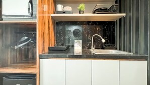A modern kitchen with a black countertop, white cabinets, a stainless steel sink, and a small potted plant on the shelf. - Cozy Stay Studio Apartment At M-Town Residence (Gading Serpong)