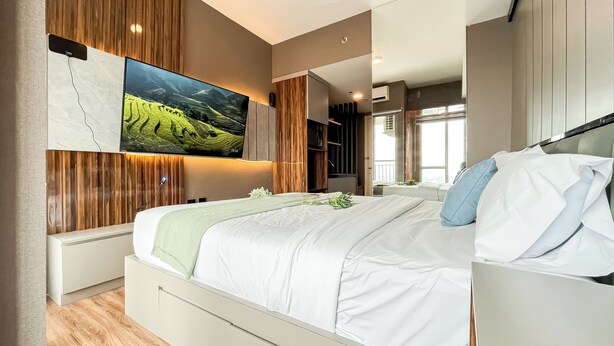 A modern bedroom with a large bed, a mounted TV, and a view of a vineyard. - Cozy Stay Studio Apartment At M-Town Residence (Gading Serpong)