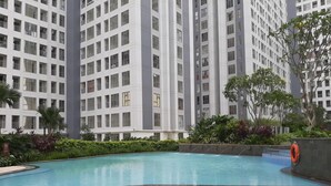 A modern high-rise building with a swimming pool surrounded by lush greenery. - Cozy Stay Studio Apartment At M-Town Residence (Gading Serpong)