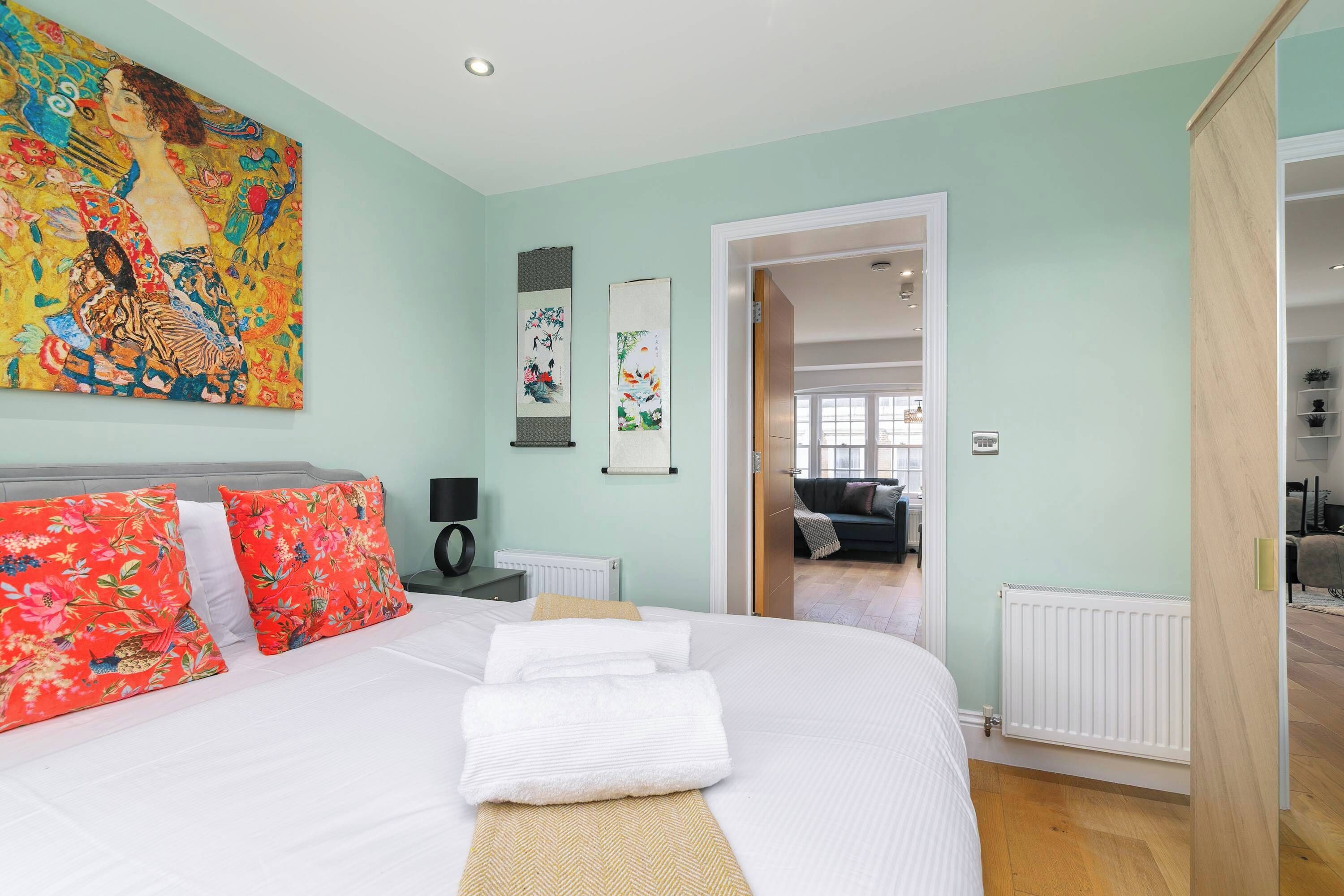 Une chambre à coucher avec un lit, des oreillers, un tableau, un radiateur et une porte donnant sur une autre pièce.