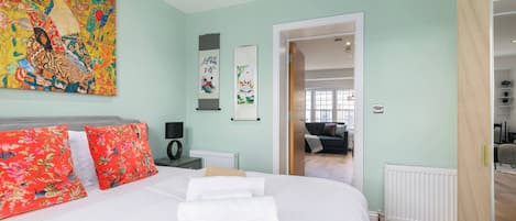 Une chambre à coucher avec un lit, des oreillers, un tableau, un radiateur et une porte donnant sur une autre pièce.
