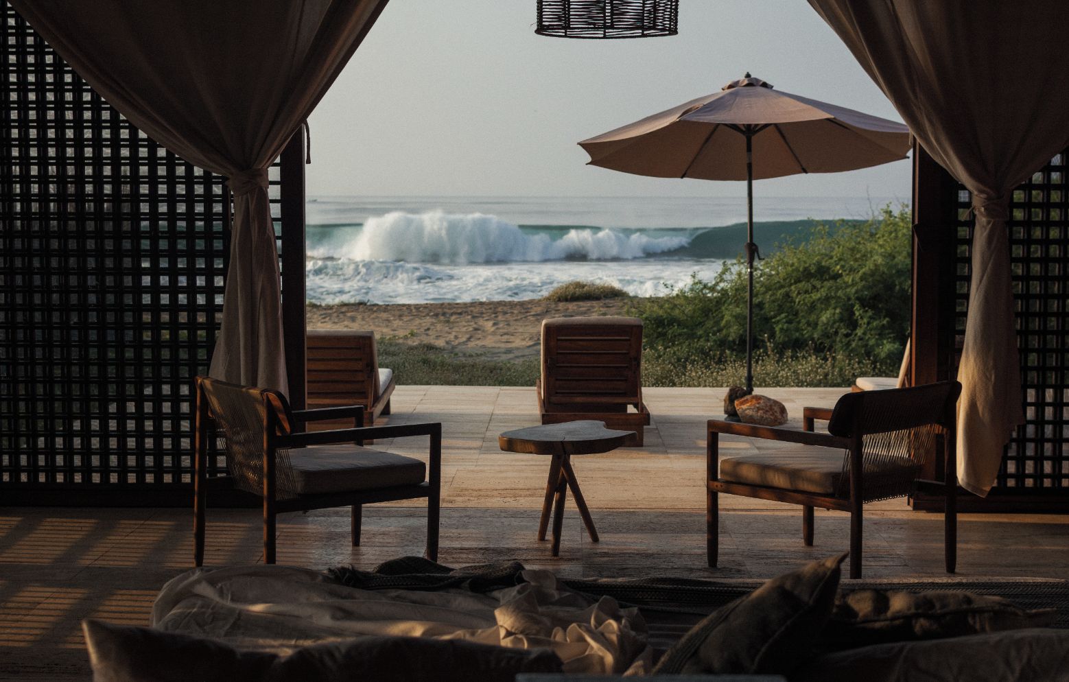 A beachside seating area with a view of the ocean, featuring wooden chairs and a table.