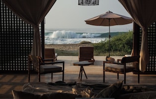 Un espacio de descanso frente a la playa, con vista al océano, con sillas de madera y una mesa.