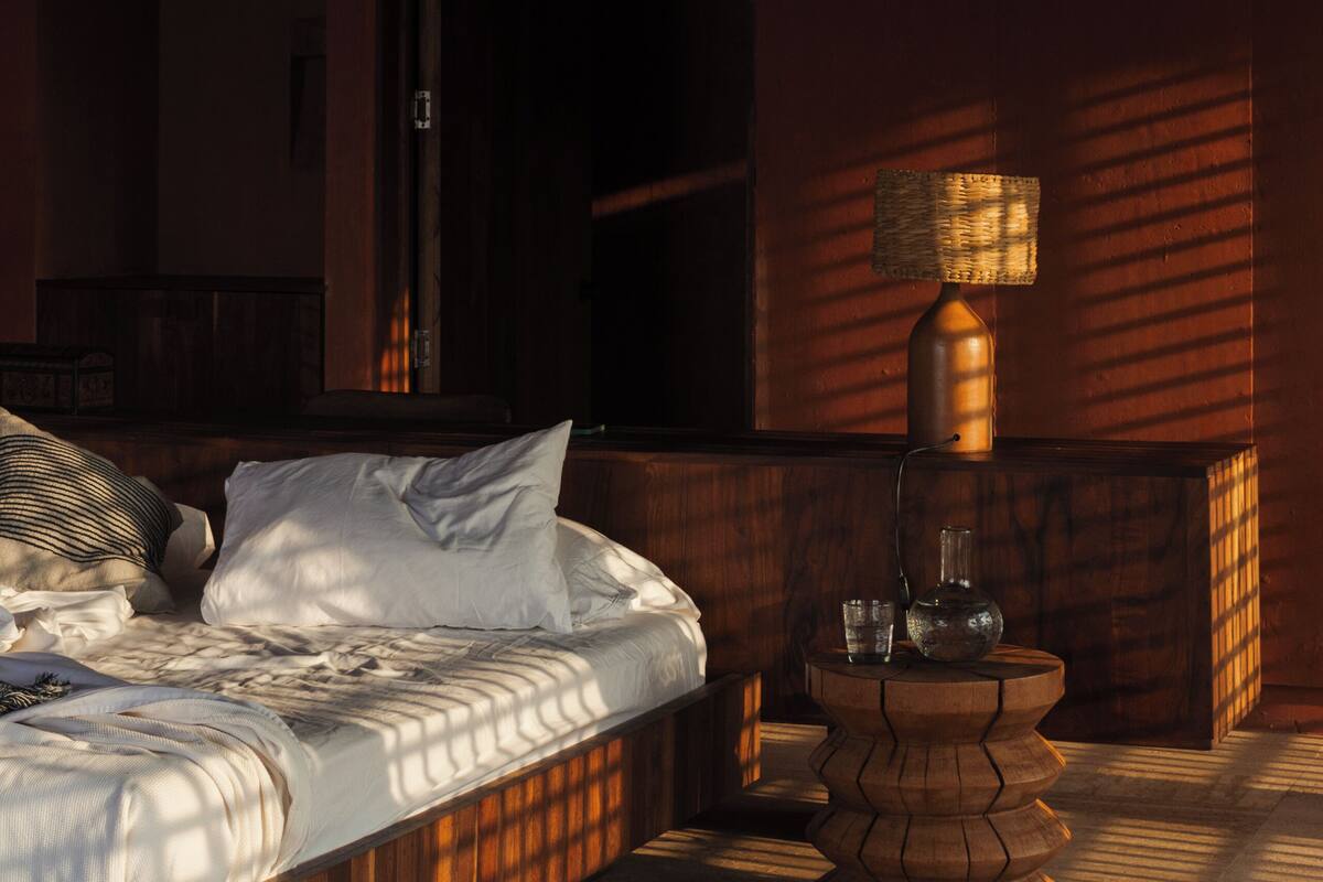 A bedroom with a bed, bedside table, and a window with a view of the outside.