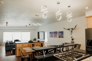A modern kitchen with a gas stove, dining table, and chairs, a living area with a sofa and TV, and a large window. - Modern 3BR Condo with Rooftop View Near Deep Ellum & Fair Park (Dallas)