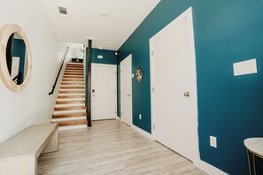 A hallway with a wooden staircase, a bench, and a door with a wall-mounted decoration. - Modern 3BR Condo with Rooftop View Near Deep Ellum & Fair Park (Dallas)