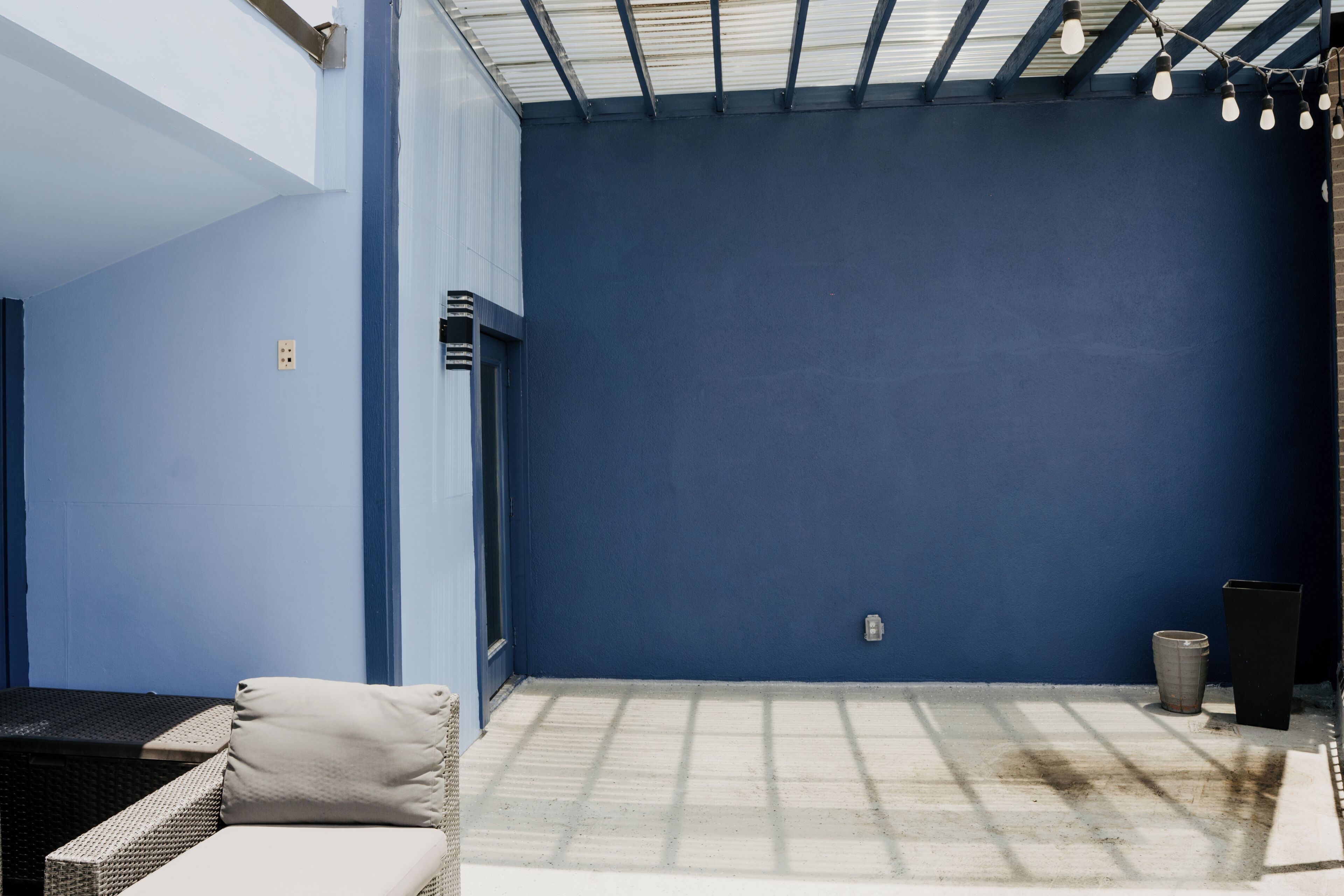Habitación con pared azul, una ventana y una puerta. Hay un aplique en el techo.