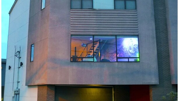 Een modern gebouw met een vlakke gevel, grote ramen en een zichtbare trap die naar een hoger gelegen verdieping leidt.
