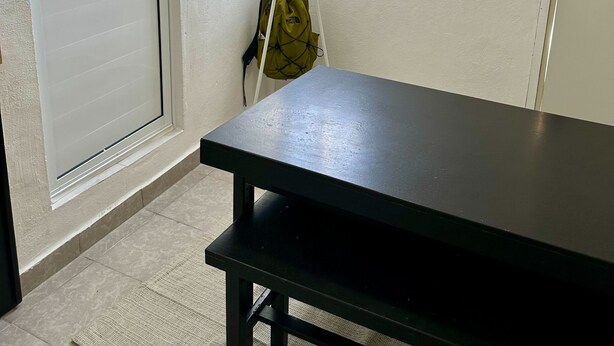 Ein Zimmer mit großem Fenster, Kleiderhaken, Tisch und Tür.