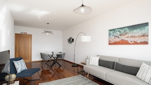Een moderne woonkamer met een bank, een eettafel met stoelen, een salontafel, een lamp en een schilderij aan de muur.