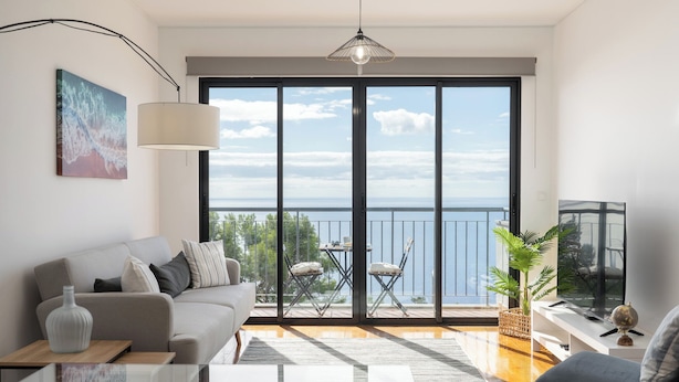 Een moderne woonkamer met een grote schuifpui die uitkomt op een balkon met uitzicht op zee.