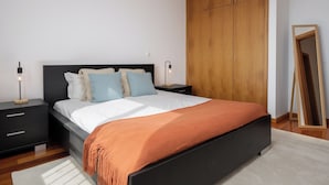 Een moderne slaapkamer met een zwart bed, wit beddengoed en een houten garderobe.