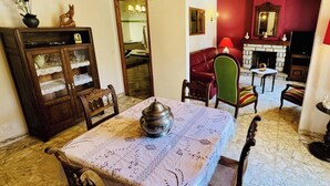 Una zona de menjador amb taula preparada per a quatre, una làmpada penjant, una llar de foc i una butaca vermella.