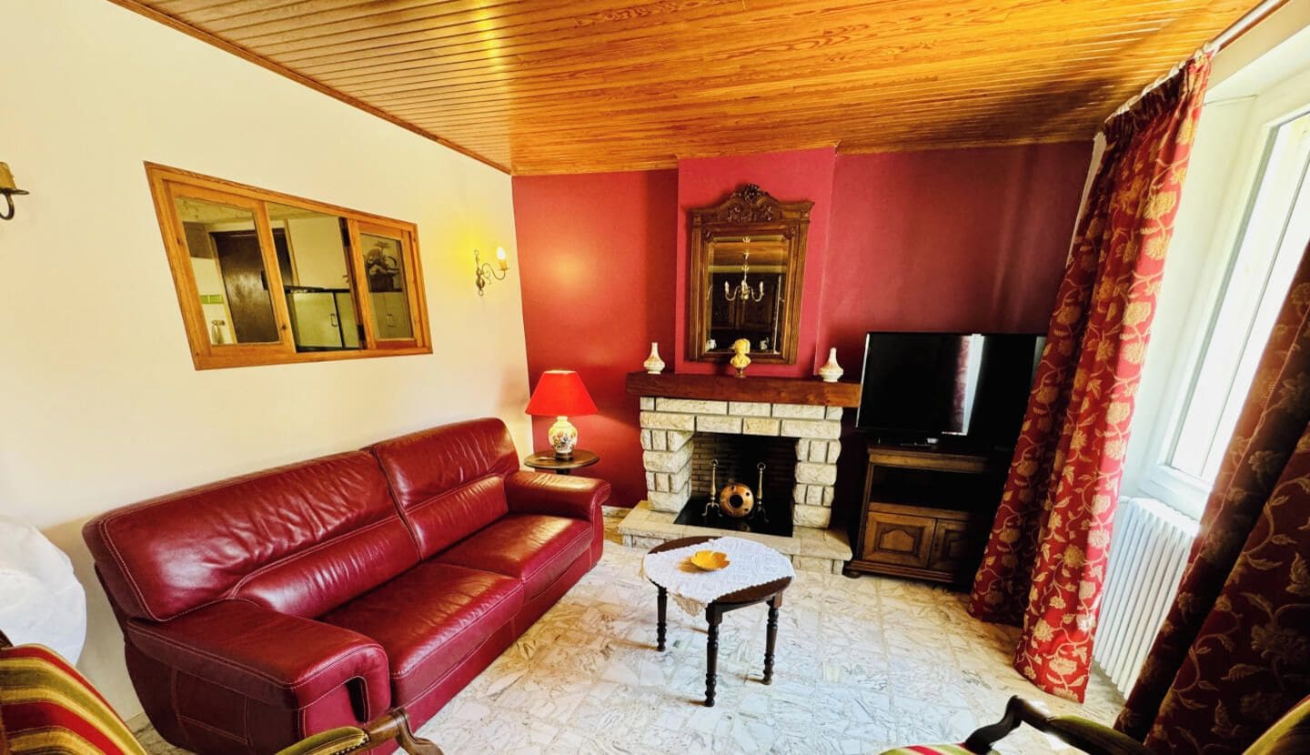 Una sala de estar con un sofá de cuero rojo, una chimenea, un televisor y una cortina estampada.