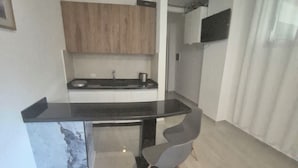 Une cuisine de taille réduite avec un plan de travail noir, des placards en bois et une seule chaise.