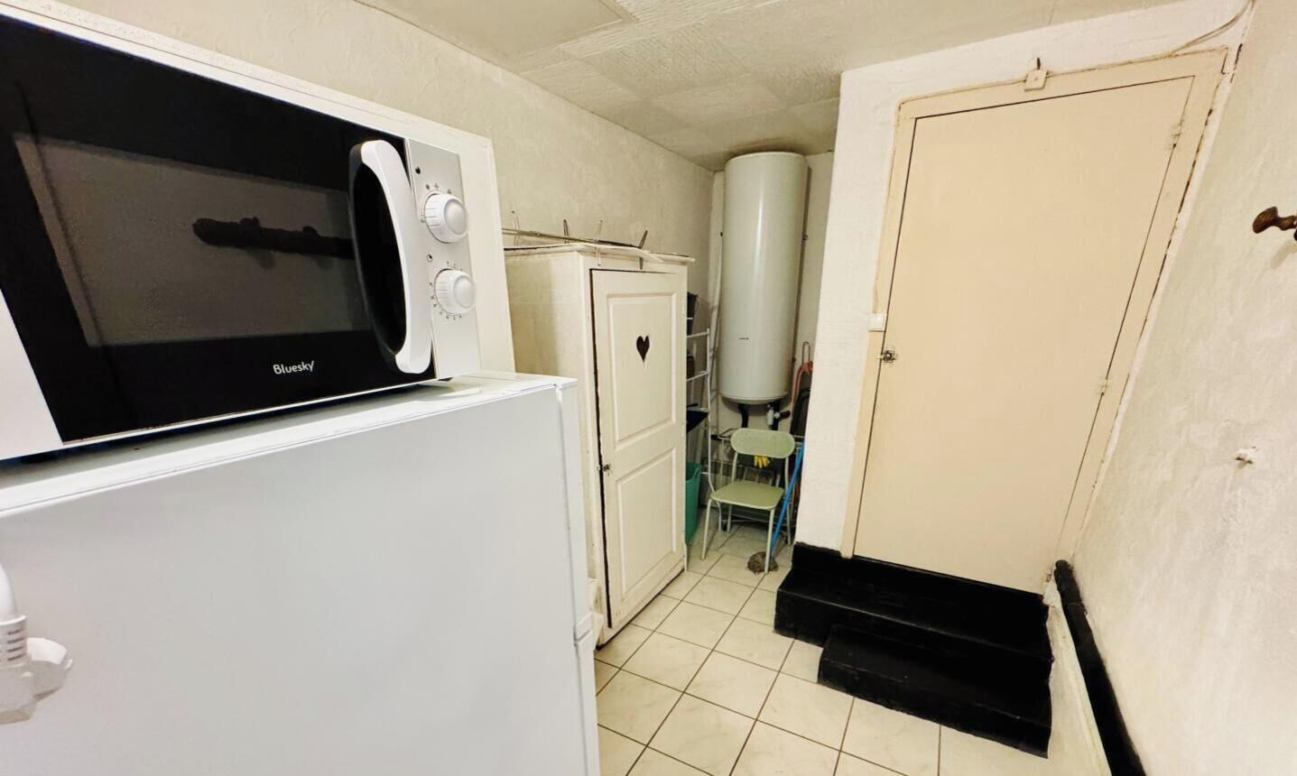 A compact kitchen with a microwave, a refrigerator, a water heater, and a door leading to another room.