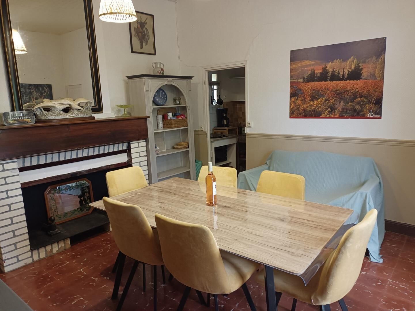 A dining area with a marble table, four chairs, a fireplace, a bookshelf, and a painting on the wall.