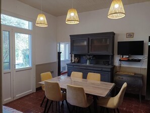 Ein Essbereich mit einem Marmortisch, vier Stühlen, einer dunklen Kommode und einem Fernseher an der Wand.