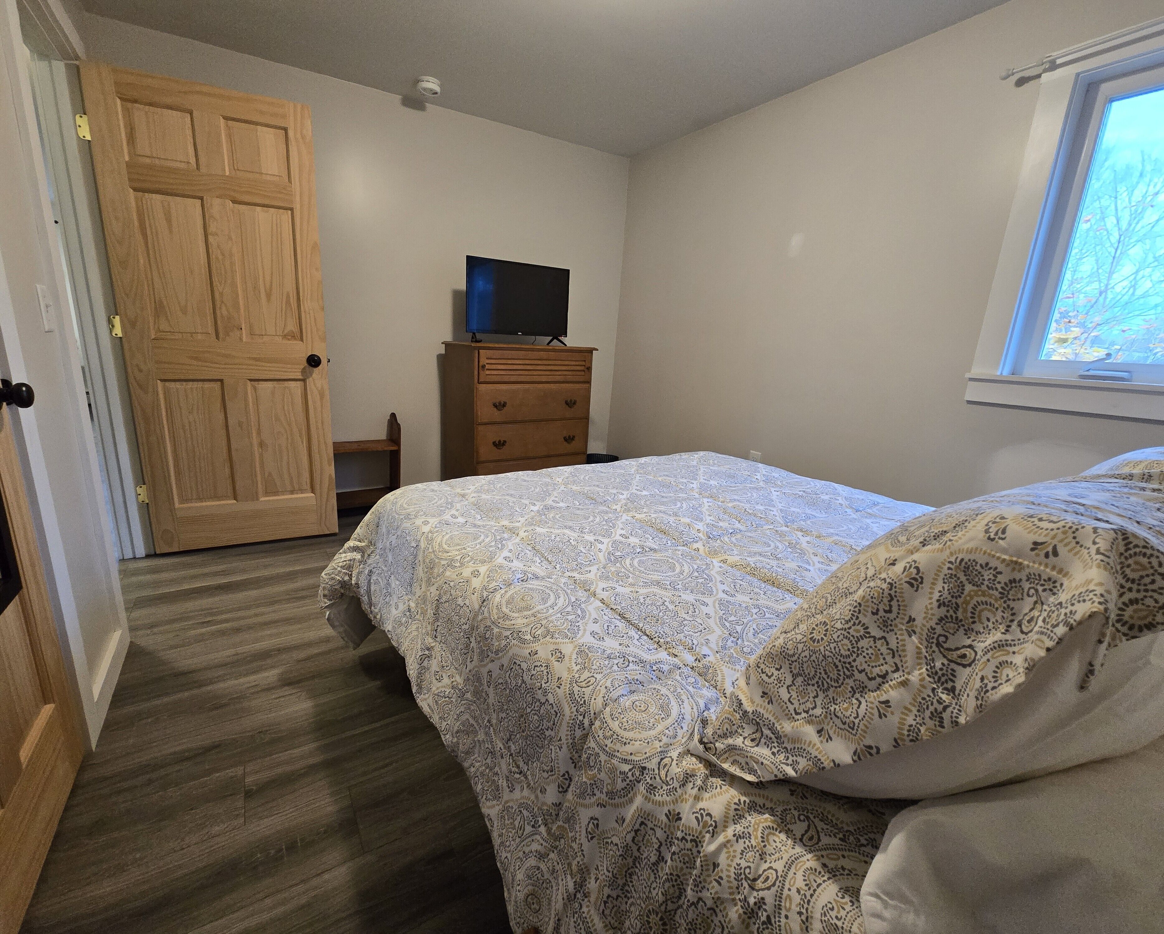 A bedroom with a bed, a dresser, a television on top, and a door.