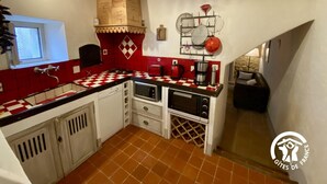 A compact kitchen with a red and white checkered backsplash, white cabinets, and a small dining area with a black table and chairs. - Aude à la Vigne - CRUSCADES (CRUSCADES)
