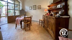 A dining area with a table set for two, a wooden cabinet with various items, and a window with a view of the outside. - Aude à la Vigne - CRUSCADES (CRUSCADES)