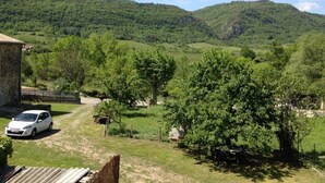 Landskab med hvide biler foran en stengård, omgivet af frodig vegetation og bakker.