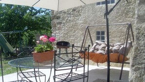 En patio med gyngestativ, et glasbord og siddepladser med hynder.