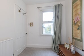 A room with a window, a radiator, a door, a curtain, a picture frame, and a decorative vase with incense sticks. - Central 3 Bedroom Home for 7 Guests (Cheltenham)