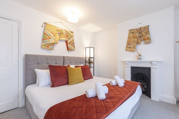 A neatly arranged bedroom with a large bed, a fireplace, and decorative items on the wall.