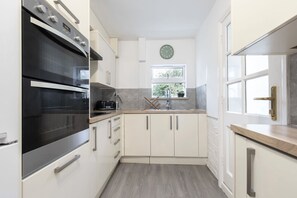 A modern kitchen with white cabinets, a black oven, a window, and a clock on the wall.