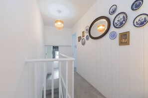 A hallway with white walls, a white railing, and a chandelier. - Central 3 Bedroom Home for 7 Guests (Cheltenham)
