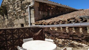 Un patio con una mesa redonda y sillas blancas, un muro de piedra y un techo de baldosas.