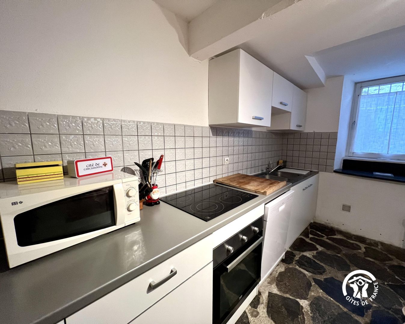 A kitchen with a microwave, stove, oven, and a stone-patterned floor.