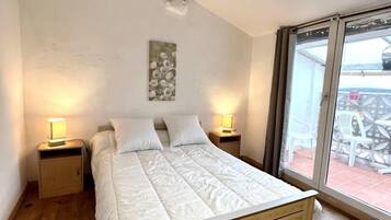 Un dormitorio con una cama de madera, dos mesitas de noche con lámparas, un techo con vigas a la vista y vistas a muebles de exterior a través de un ventanal.