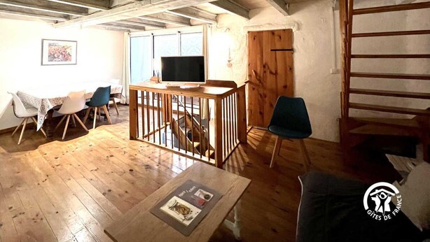 Una habitación rústica con pisos de madera, un televisor sobre una mesa de madera, una escalera y una silla.