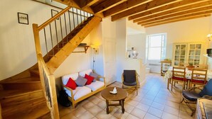 A cozy interior with a wooden staircase, a sofa with cushions, a dining table with chairs, and a kitchen area. - Gite du Cammas Blanc (VILLEPINTE)