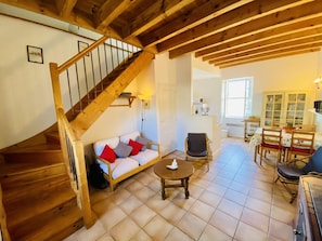 A cozy interior with a wooden staircase, a sofa with cushions, a dining table with chairs, and a kitchen area. - Gite du Cammas Blanc (VILLEPINTE)