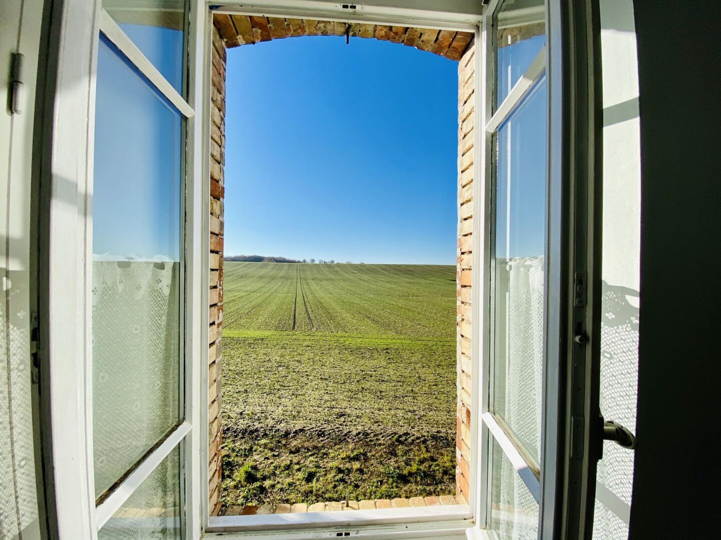 An open window with a view of a green field and a clear blue sky.