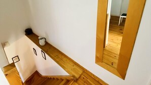 A narrow staircase with wooden steps leading to a landing. A white wall with a mirror and a small table with a cup and a book are visible. - Gite du Cammas Blanc (VILLEPINTE)