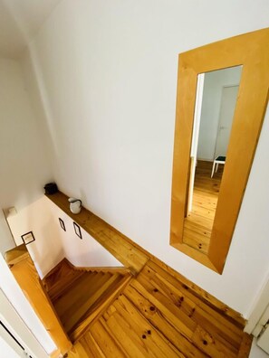 A narrow staircase with wooden steps leading to a landing. A white wall with a mirror and a small table with a cup and a book are visible. - Gite du Cammas Blanc (VILLEPINTE)