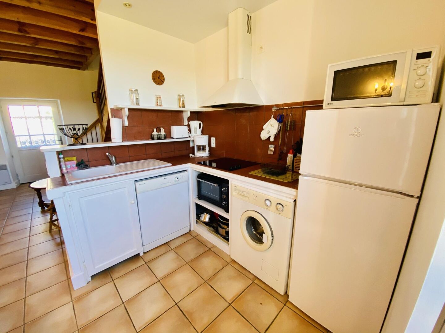 A compact kitchen with a dishwasher, washing machine, microwave, and a refrigerator.