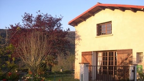 A two-story building with a red roof, a gated entrance, and a garden with flowers. - L'Olivier - QUILLAN - Gîte (QUILLAN)