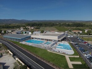 Ein Schwimmbadkomplex mit mehreren Pools und einem überdachten Bereich, neben einer Straße und einem Parkplatz.