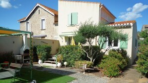 Une maison à deux étages avec un patio, un petit jardin et un chien.